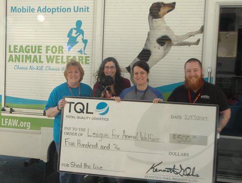Four People Smile With a Giant TQL Check
