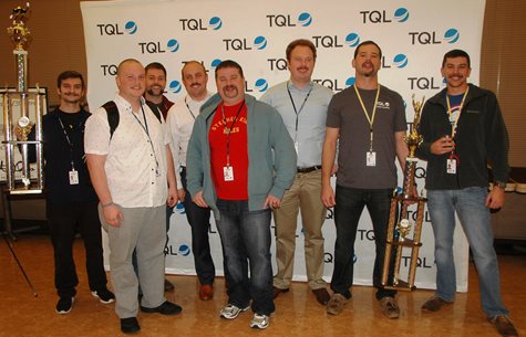 A Group Of Men Smiling With Trophies In Front Of A TQL Background