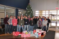 Group Of People Smiling In Front Of A Christmas Tree With Gifts