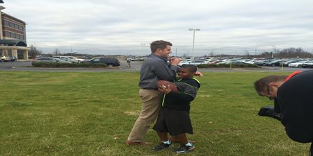 A Young Boy Holding A Football And Hugging His Big Brother On Film In Front Of The TQL Office