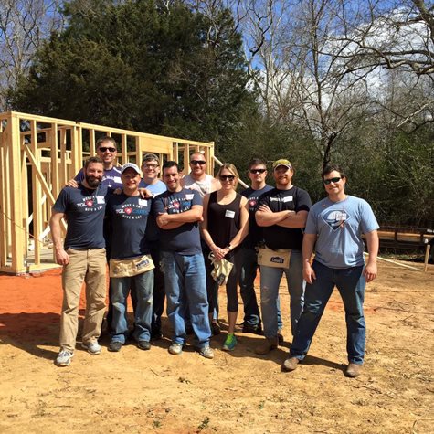 Employees with TQL Cares Shirts On Smile In Front Of The Wooden Foundation Of A House