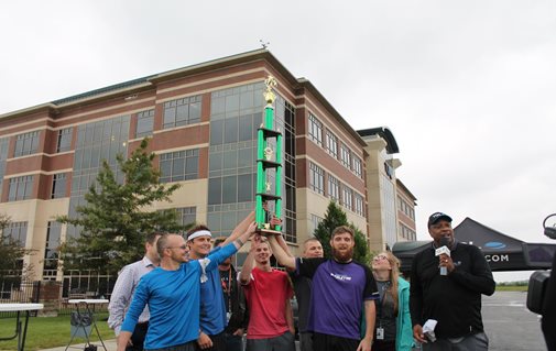 A Group Of People Raising A Trophy Together In Front Of The TQL Building