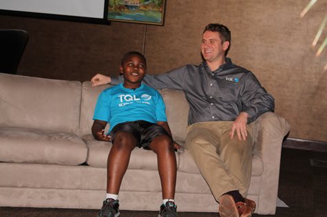 A Big And Little Sitting On A Couch With Their Arms Around One Another Wearing TQL Gear