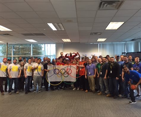 TQL Charlotte Group Smiling With An Olympics Logo Banner