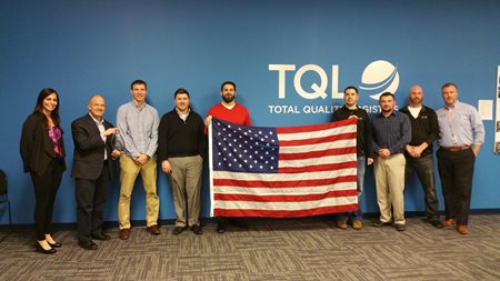 Group Of TQL Employees Holding An American Flag In Front Of A Blue TQL Wall