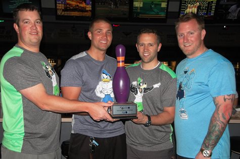 Four Men Holding A Bowling Pin Shaped Trophy At A Bowling Alley