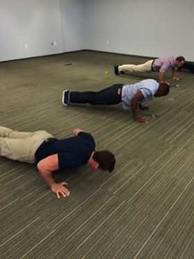 Three men doing push ups in empty office room
