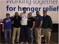 Group Of TQL Employees Posing In Front of A Sign That Says Working Together For Hunger Relief