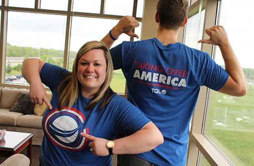 Two TQL Employees Pointing To Their Logos On Their Matching Blue TQL Shirts