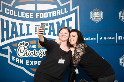 Two women taking selfie in front of College football hall of fame backdrop