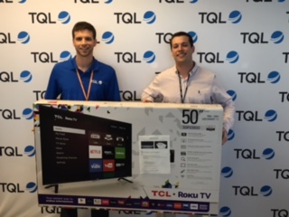Two Employees Posing In Front Of A TQL Wall With A New Roku TV