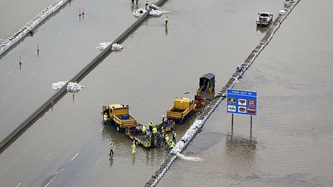 A Highway Flooded With A Couple Trucks And A Sign Sticking Out Of The Water