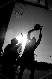 Black and white action shot of two men at basketball net