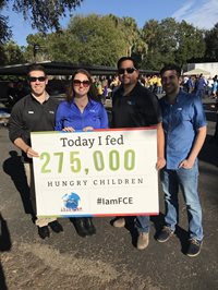 Four People Smiling Holding A Sign Saying How many Children They Fed Today