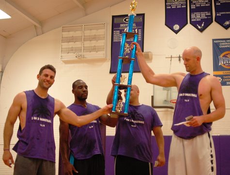 Four Men On A Basketball Court Holding Up A Large Trophy Together