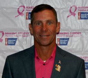 Gary Carr Smiling In Front Of Breast Cancer Ribbons And Wearing A Pink Shirt